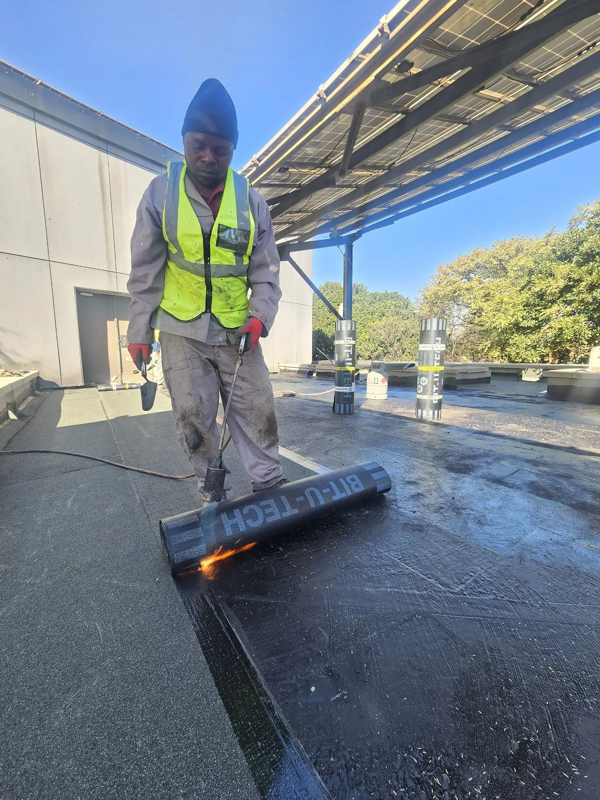 Technician applying torch-on waterproofing membrane during flat roof restoration and waterproofing work