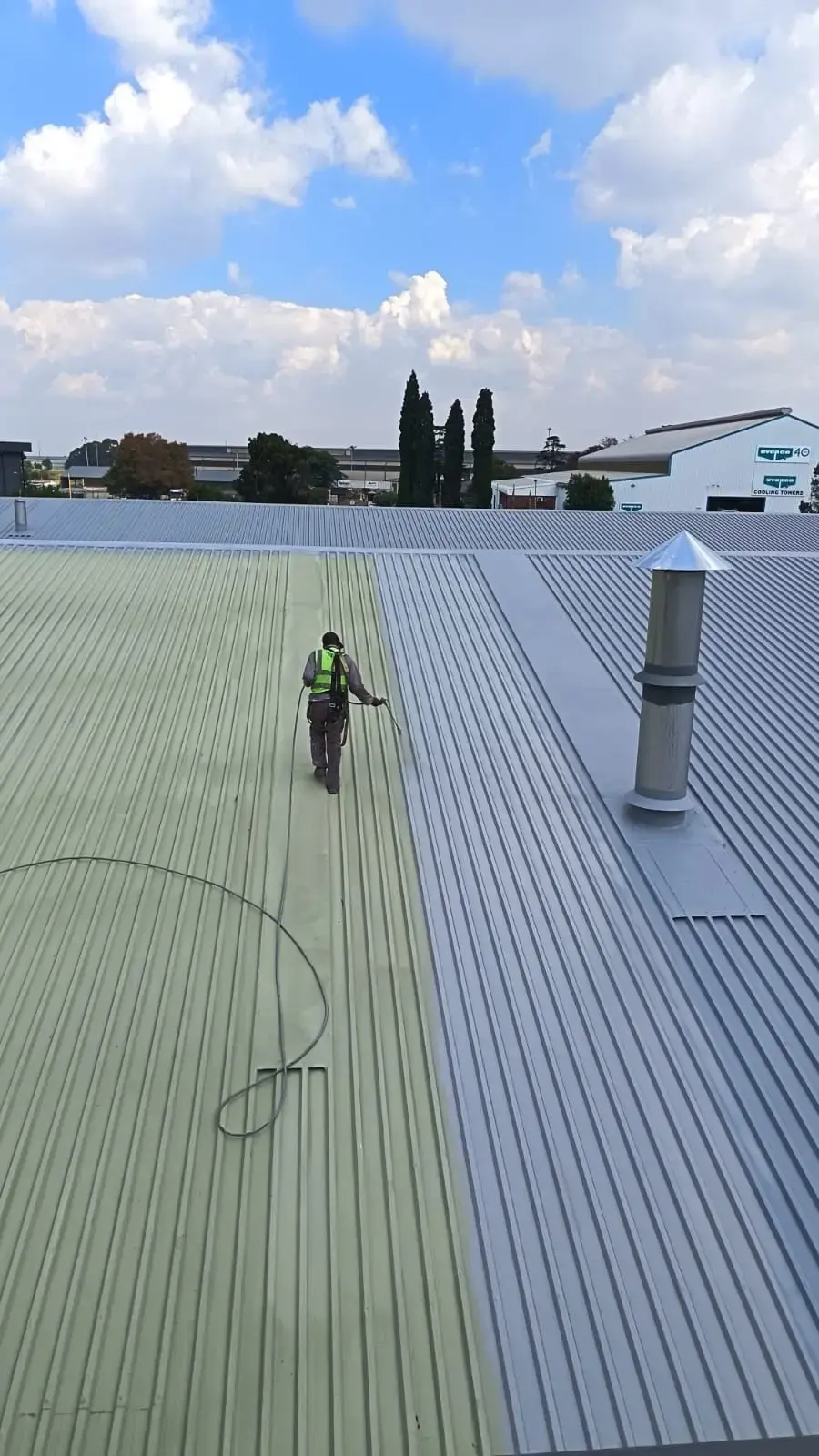 Worker applying protective coating during metal roof restoration on an industrial roof