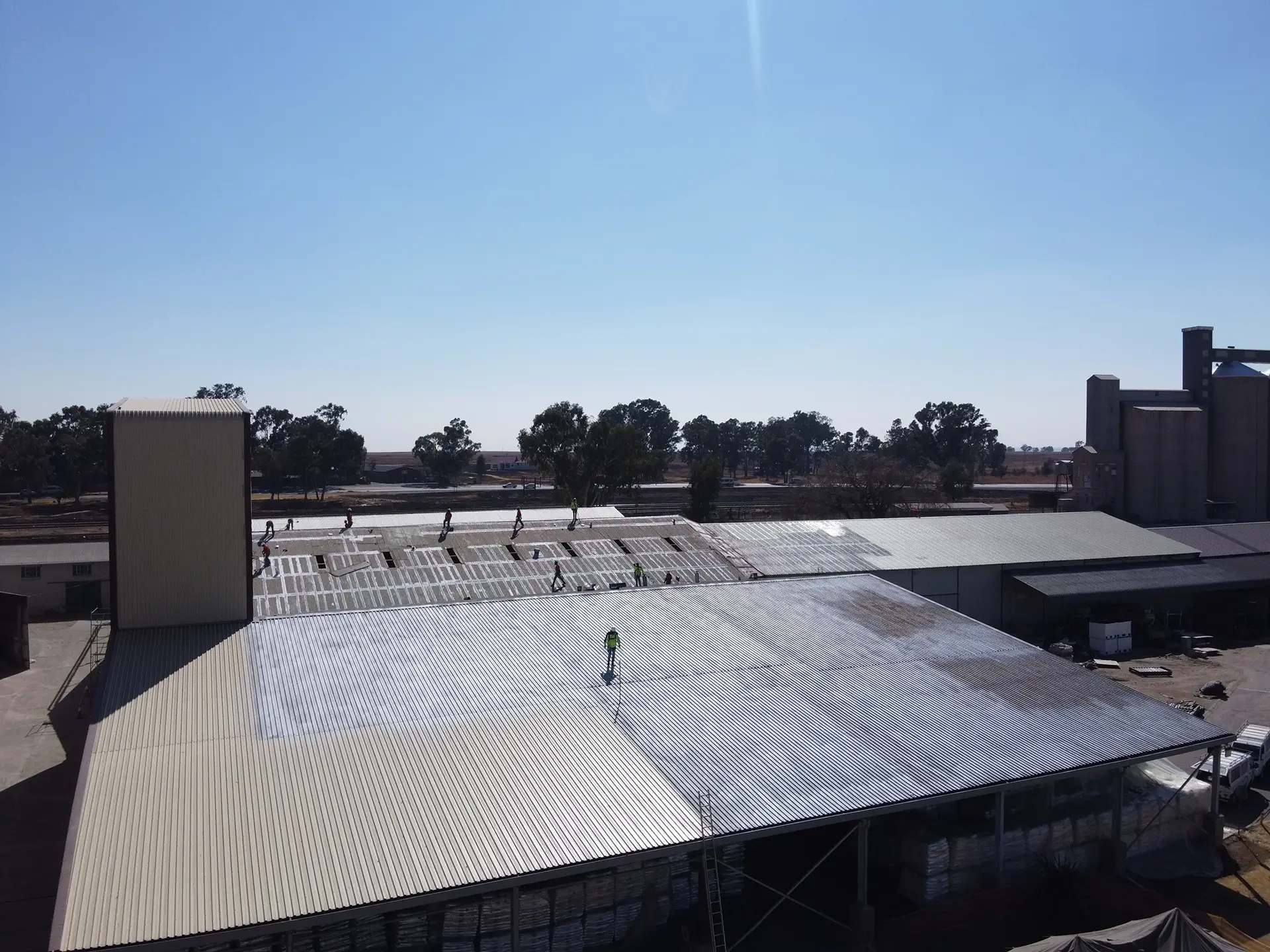 Workers carrying out roof restoration on a large industrial factory roof with safety gear and access equipment